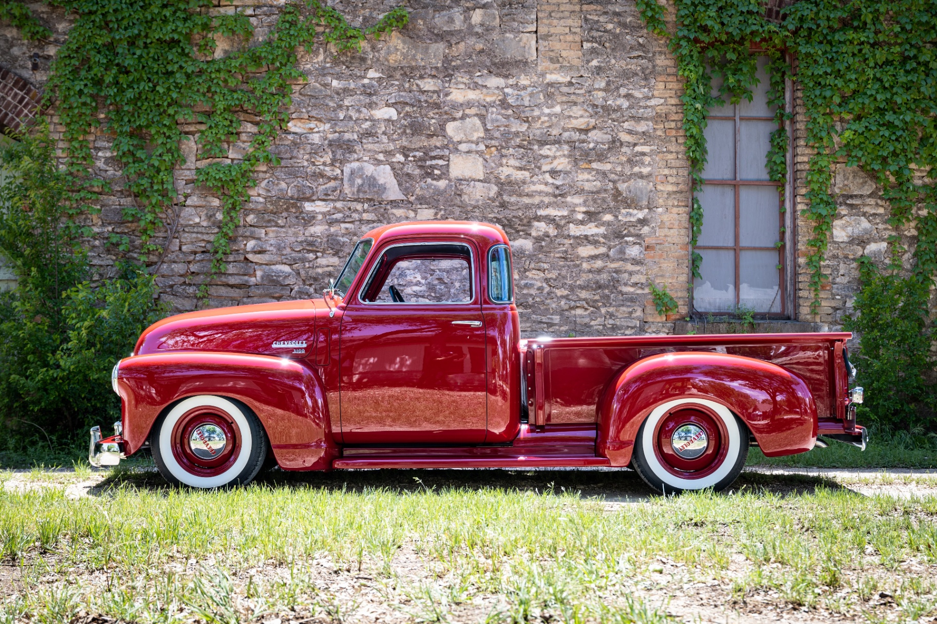 Passenger-side profile — stance and wheel-to-fender relationship shot against ivy-covered stone.