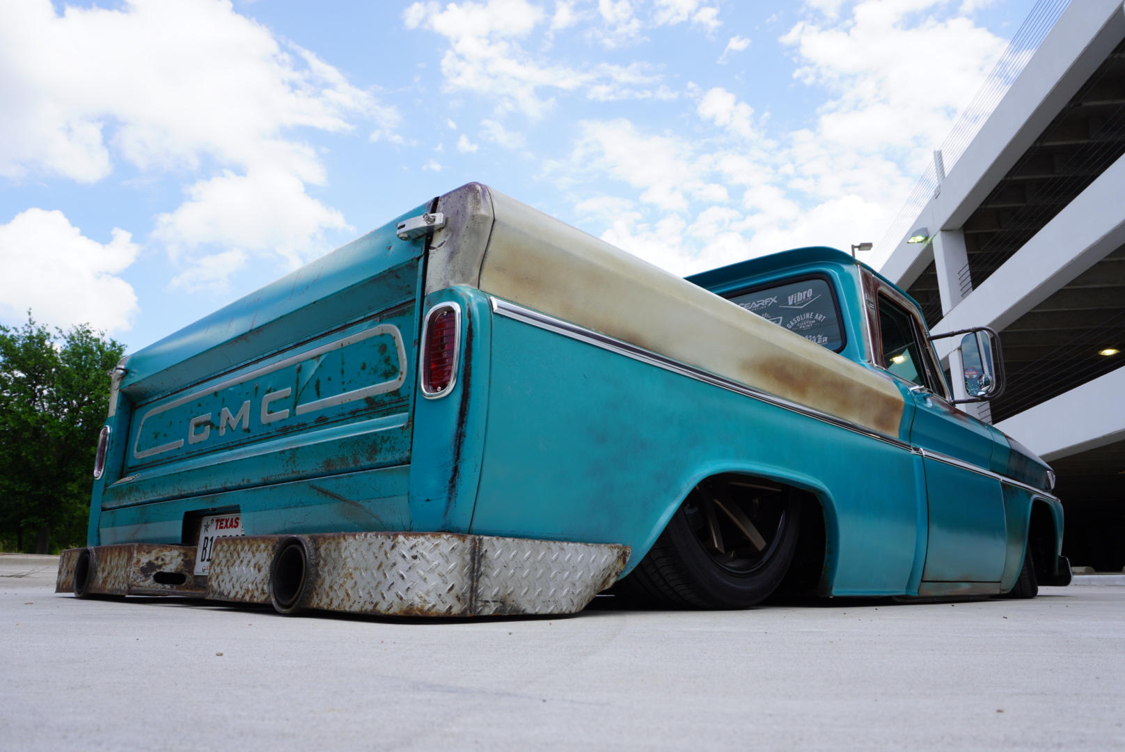 Rear worm's-eye view against a Texas sky — GMC tailgate, laid-out stance, and the truck's true proportions from ground level.