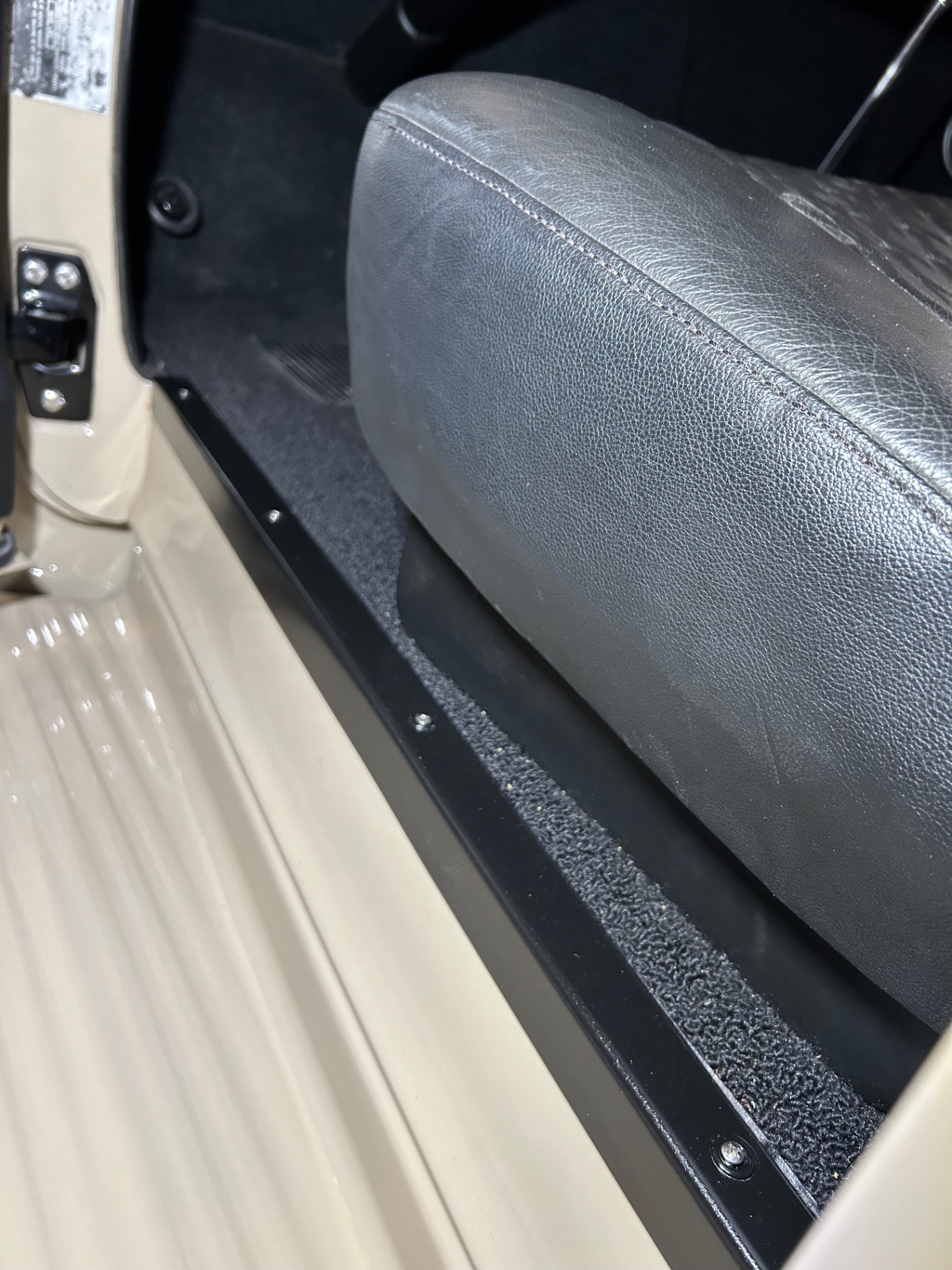 Sill and kick detail — diamond-stitched seat bolster, black sill plate, tan floor pan.