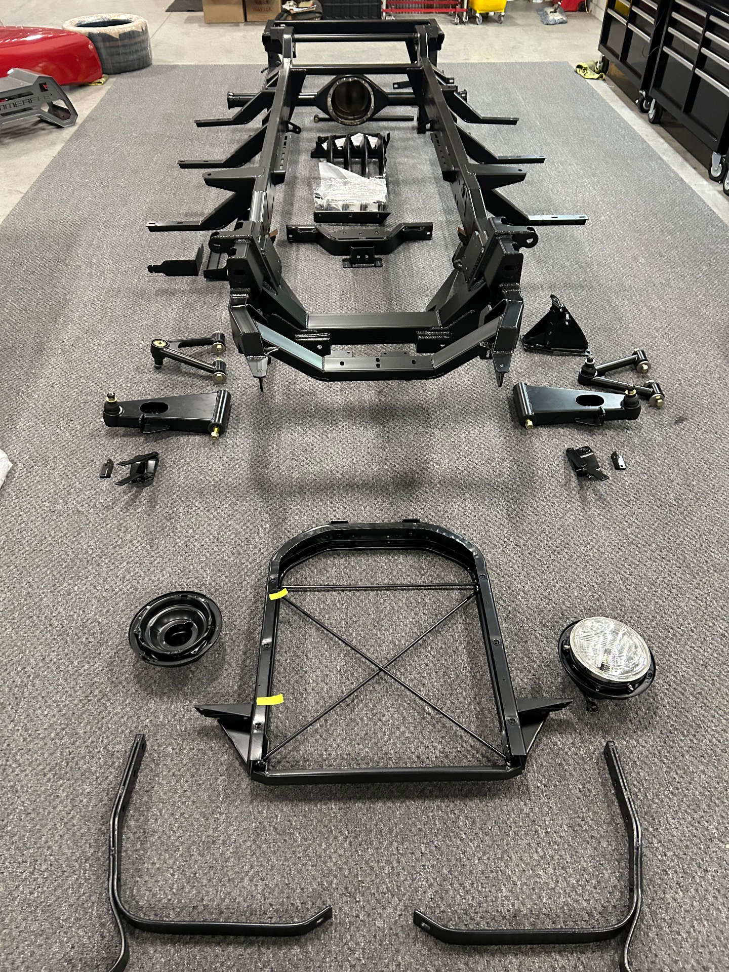 Powder-coated SPEC chassis and front sheet metal support laid out on the shop floor with control arms and hardware, staged before reassembly.
