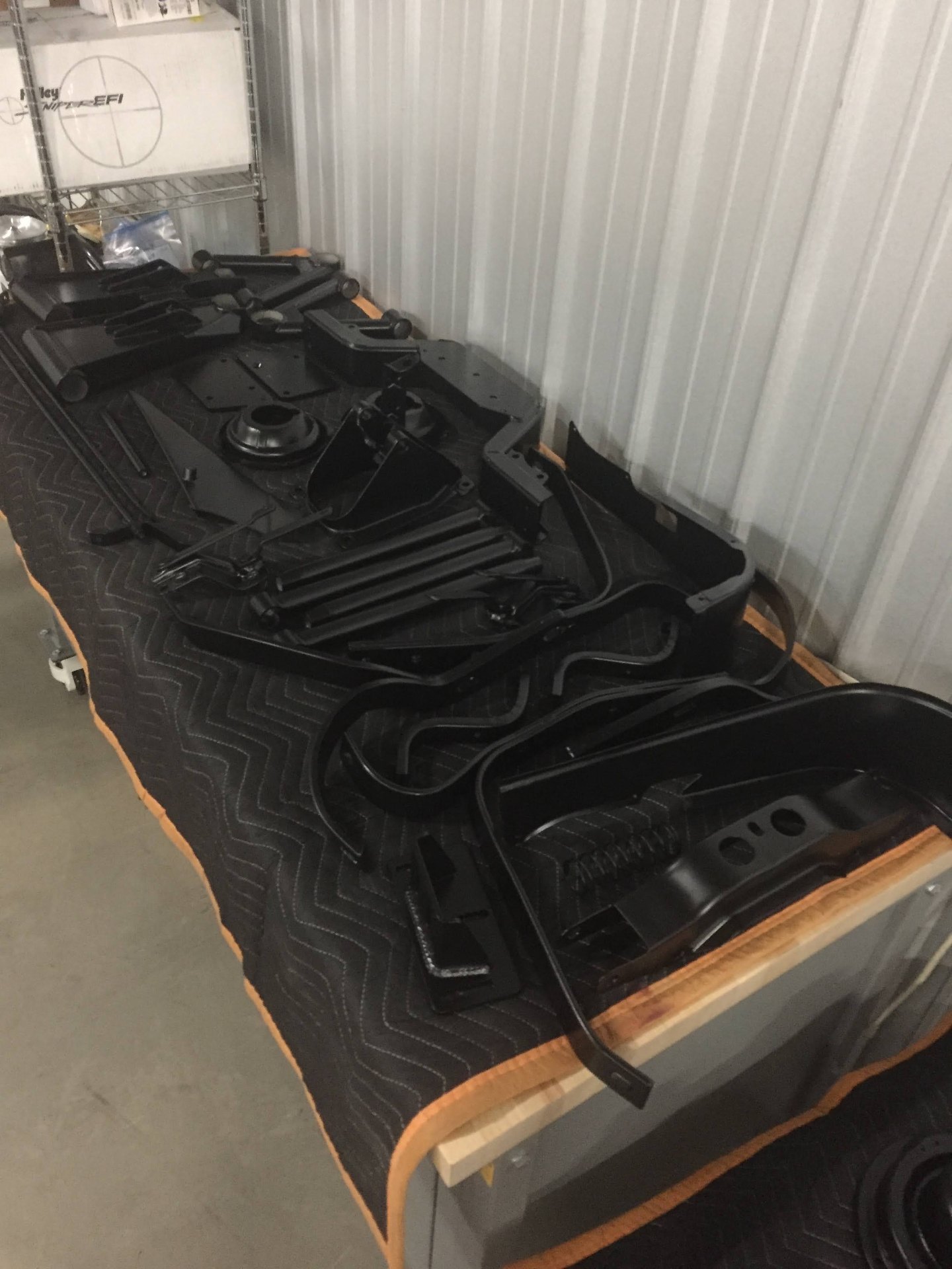 Fresh powder-coated chassis parts staged on the bench — crossmembers, brackets, and hardware laid out satin black and ready to bolt back together.
