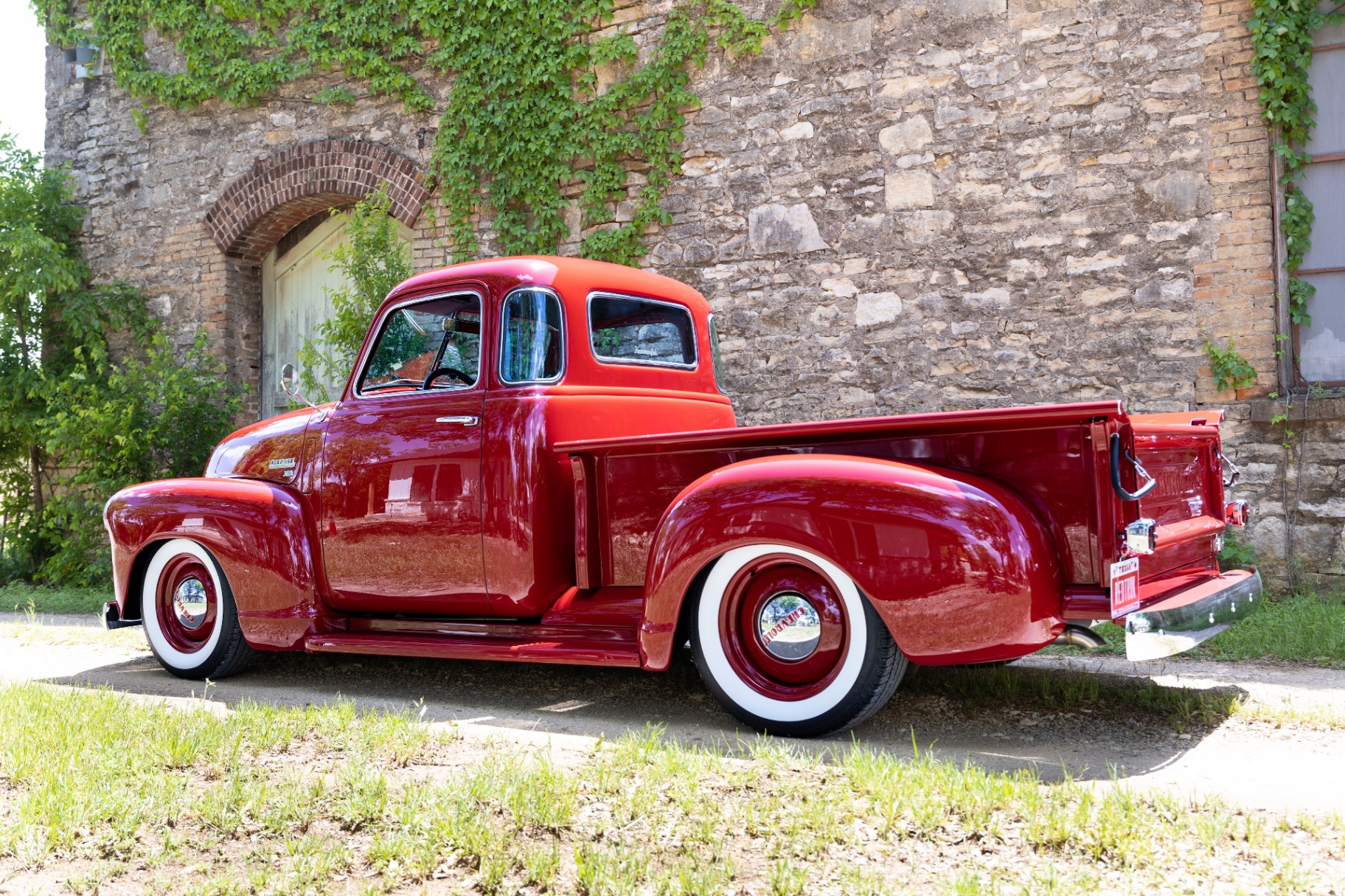 Rear three-quarter — Texas plate, chrome bumper, and the painted bed sides catching the sun.