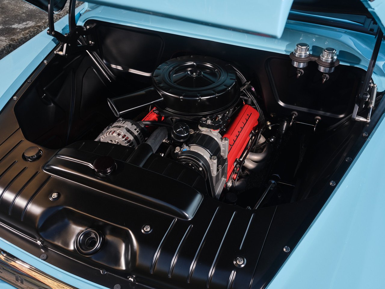 Overhead engine bay — red valve covers under a black air cleaner, smoothed and painted firewall, GM through and through.