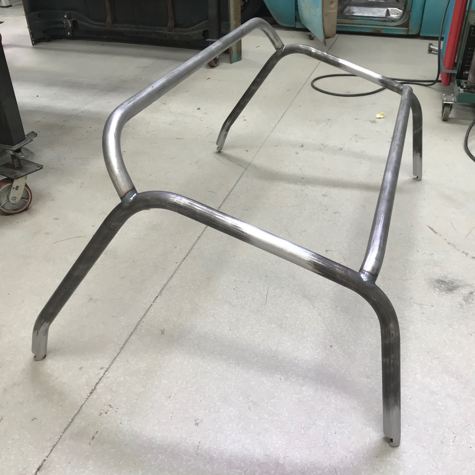 Roll cage laid out on the floor — main hoop, A-pillar bars, and harness bar ready to go in.