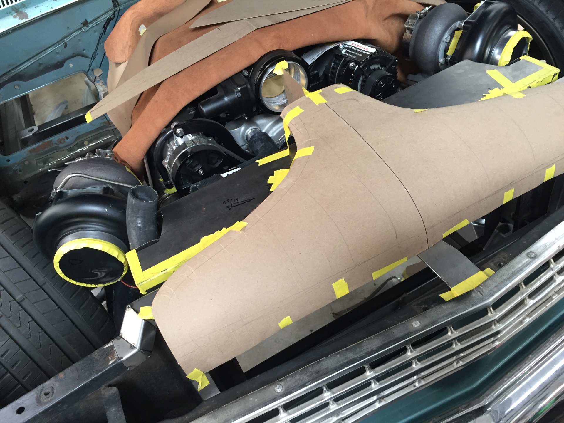 Cardboard mockup of the funnel and plenum taped in place under the hood to confirm clearance to the turbos and welding blankets protecting the paint.