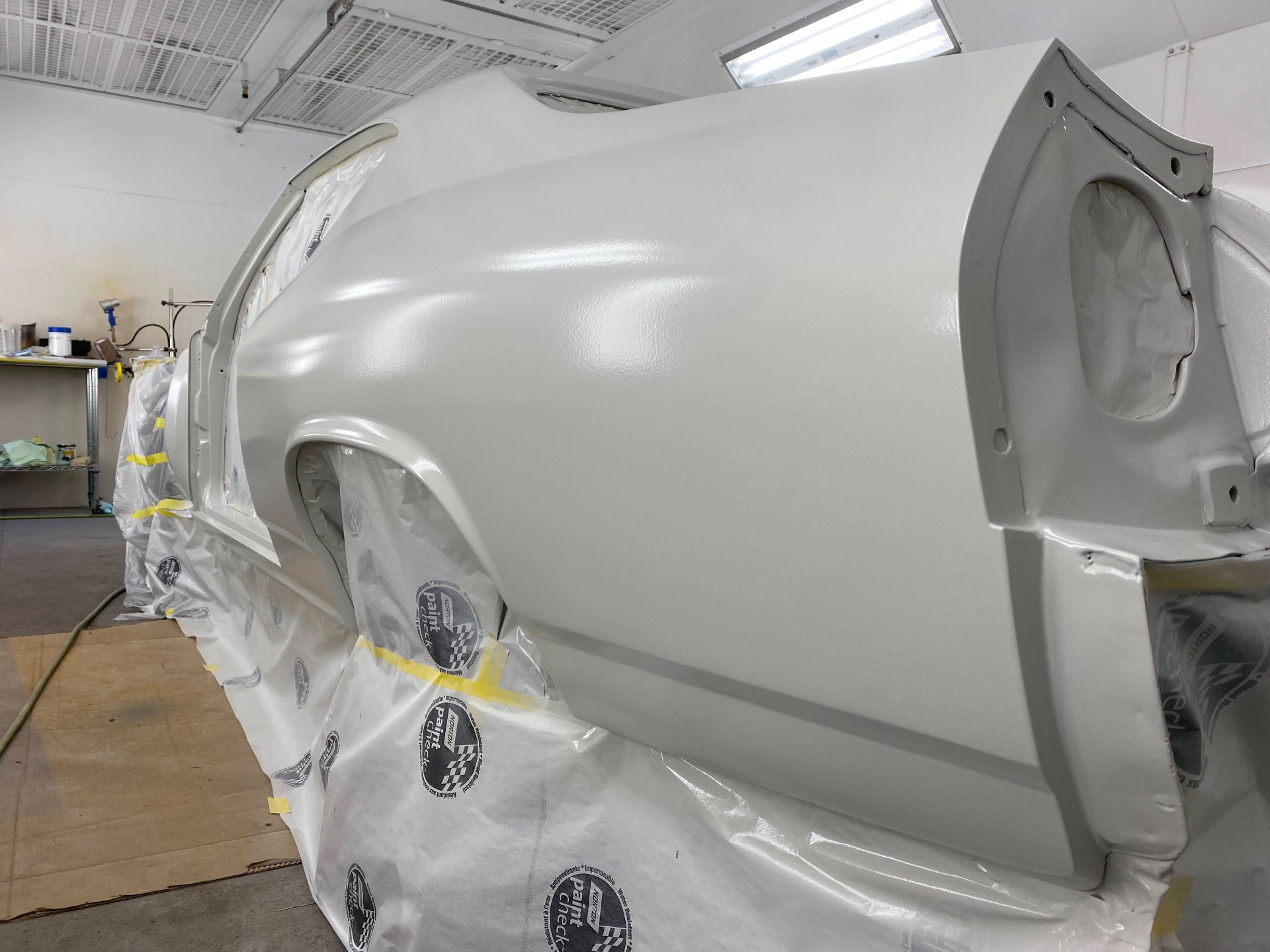 Quarter panel and rear glass area — pearl white laying flat under the booth lights.