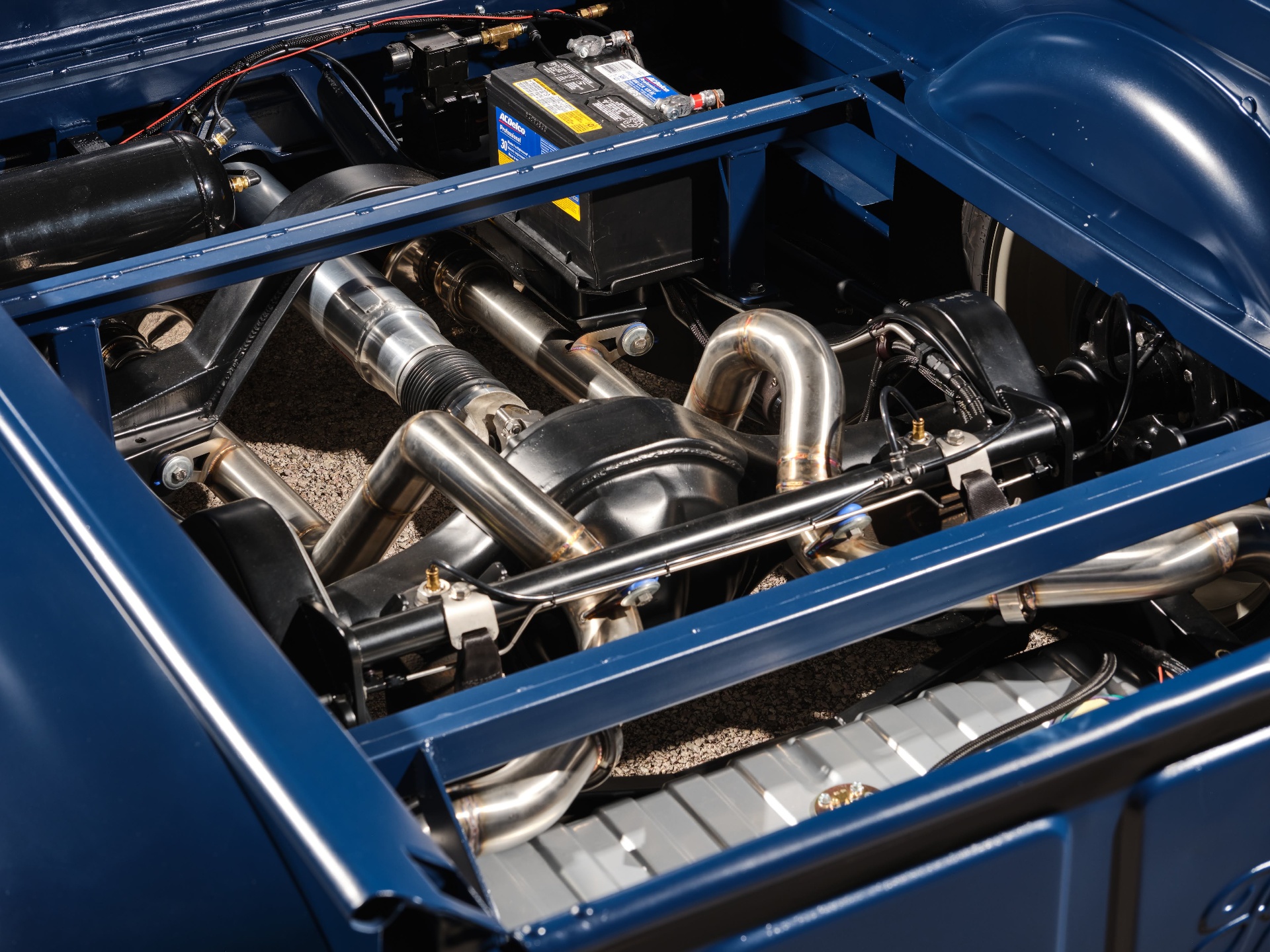 Underside view — custom air-ride chassis, air tank, valves, and battery packaged in the bed area over the hand-built stainless exhaust.
