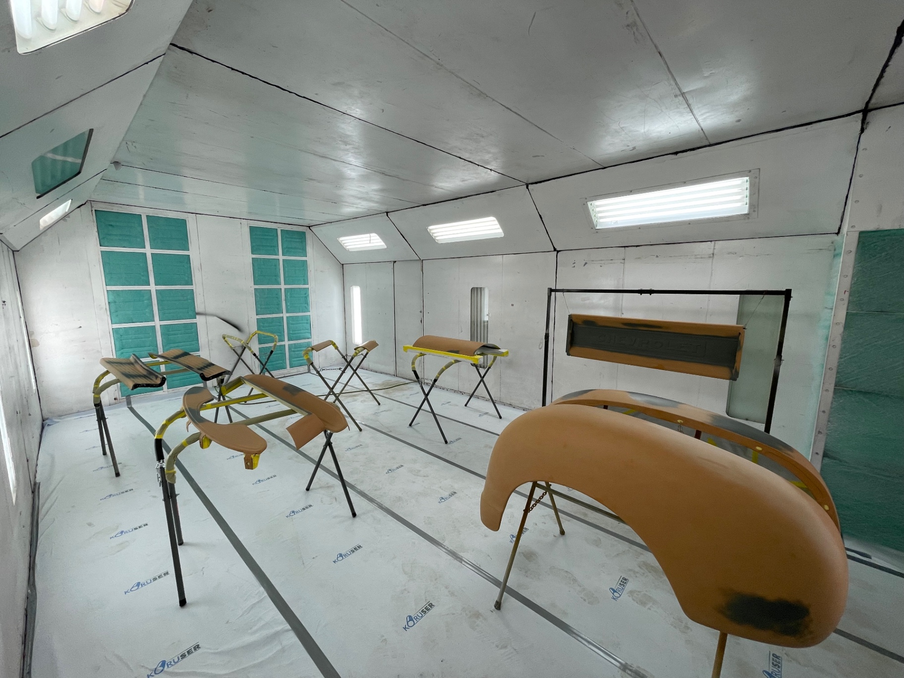 Booth full of primered panels — fenders, running boards, tailgate, and grille surround staged for blocking.