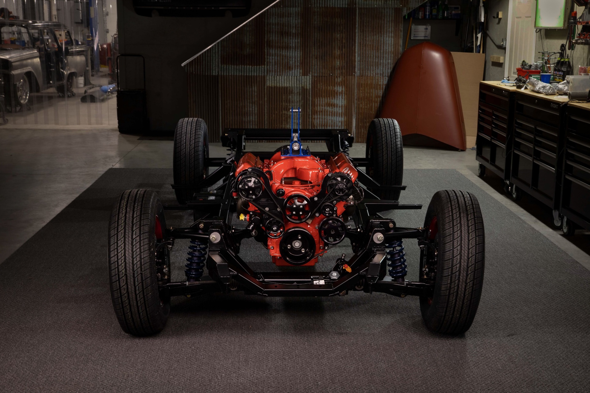 Chassis head-on — accessory drive, coilovers, and blacked-out control arms framing the powder-coated LS block.