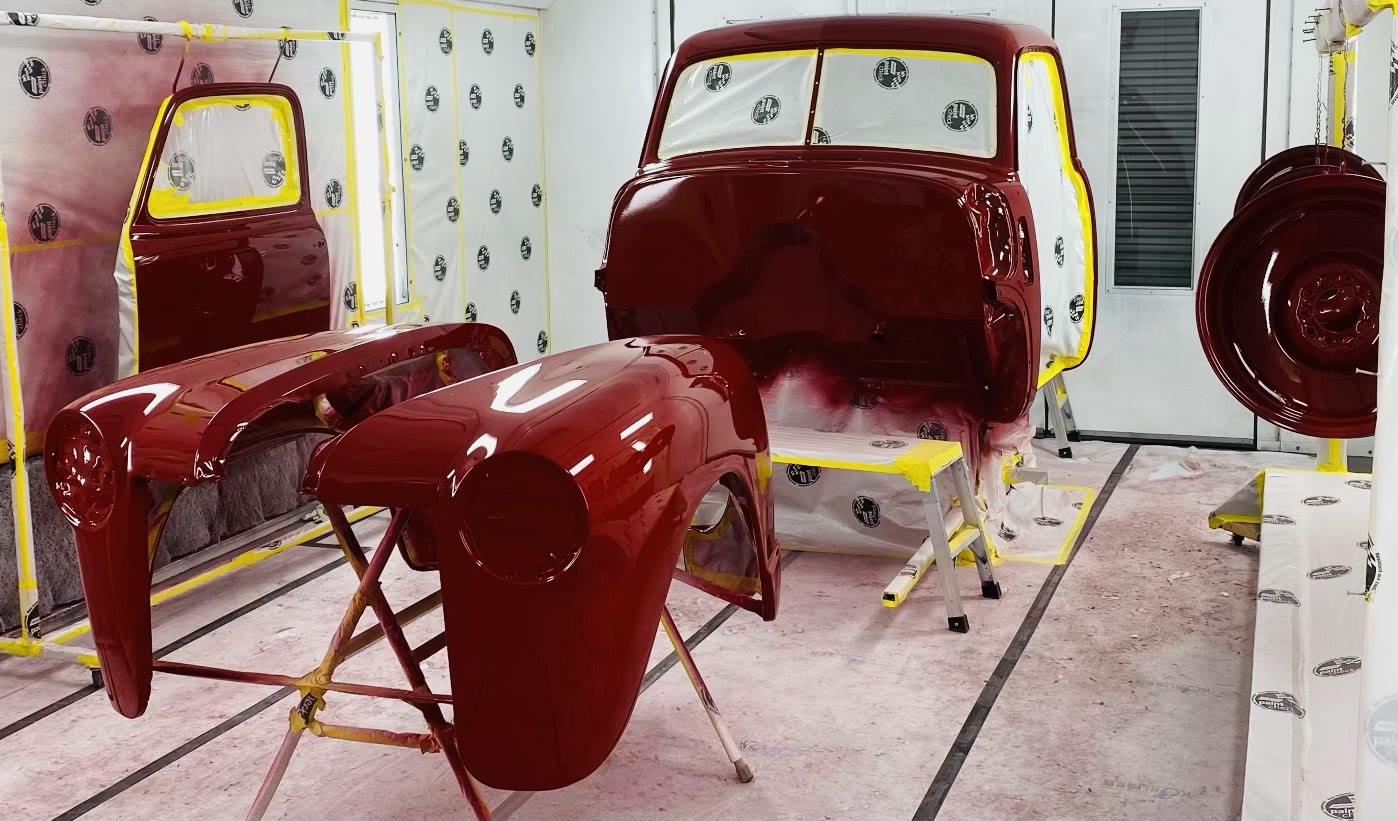 Front fenders staged in front of the cab, a wheel hanging at right — every part painted off the truck so nothing hides an unfinished edge.